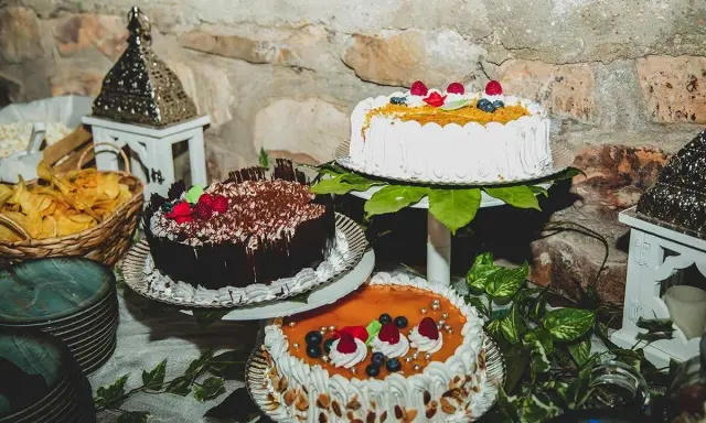Mesa dulce boda casera con tres pasteles decorados con frutas y chocolate. Hay también cestas con patatas fritas y adornos rústicos.