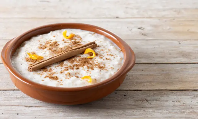 Un tazón de arroz con leche cremoso, espolvoreado con canela y adornado con cáscara de naranja y una rama de canela.