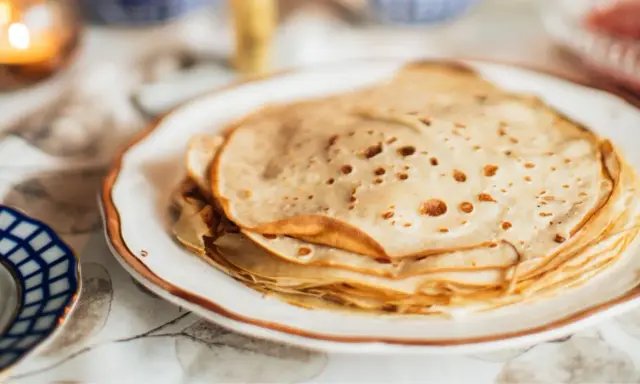 Una pila de masa crepes doradas y finas en un plato blanco.