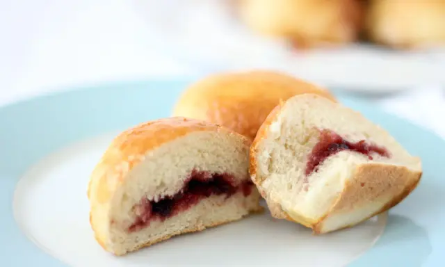 Dos bollos dorados, uno cortado, revelan un relleno de mermelada de fresa. ¡Un dulce bocado!