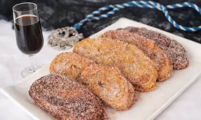 Torrijas cubiertas de azúcar y canela, listas para disfrutar. Un delicioso pan para torrijas, acompañado de una copa de vino dulce.