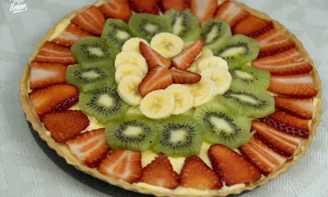 Deliciosa tarta con decoración de tartas con frutas: fresas, kiwi y plátano, dispuestas en círculos concéntricos sobre una base cremosa.