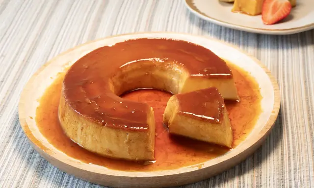 Un delicioso flan de leche condensada con caramelo líquido, servido en un plato de madera.