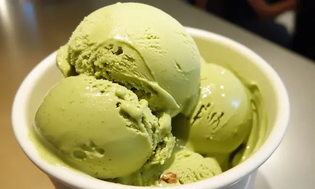 Un tazón blanco lleno de cremoso helado de pistacho, con trozos visibles de pistacho en algunas bolas.