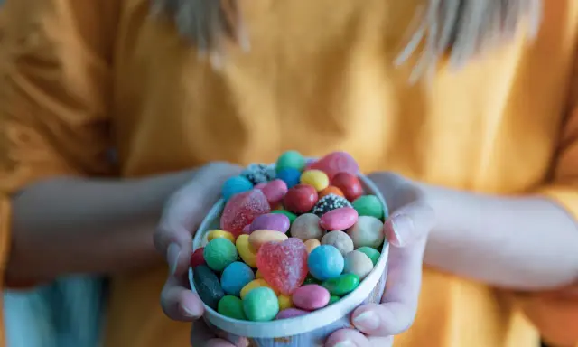 Manos sostienen un cuenco lleno de chuches saludables para niños: gomitas de corazón, bolitas de colores y más.
