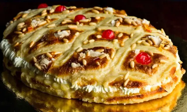 Deliciosa coca de Sant Joan rellena de crema, decorada con piñones, cerezas rojas y azúcar.