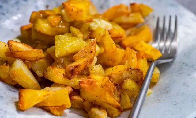 Patatas fritas al horno doradas y crujientes, sazonadas con especias, listas para disfrutar con un tenedor.