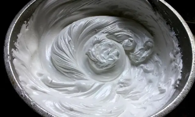 Merengue italiano recién batido en un bol metálico, con remolinos suaves y sedosos que invitan a probar su dulzura.