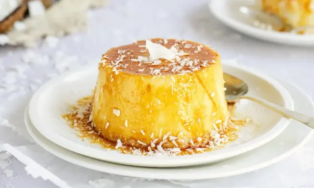 Delicioso flan de coco con caramelo líquido y coco rallado, servido en un plato blanco con una cuchara dorada.