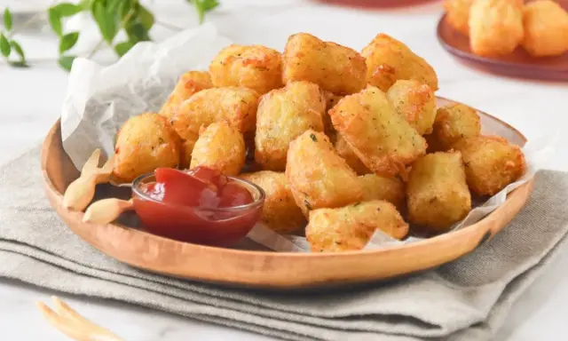 Tater tots dorados y crujientes servidos en un plato de madera con ketchup.