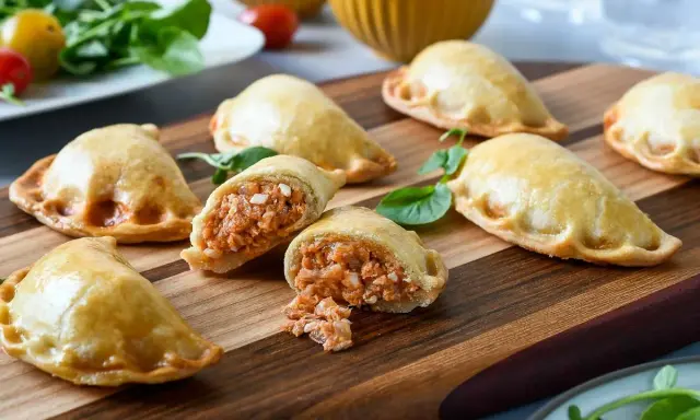 Empanadillas caseras doradas y crujientes, una rellena muestra su sabroso interior. Perfectas para compartir.