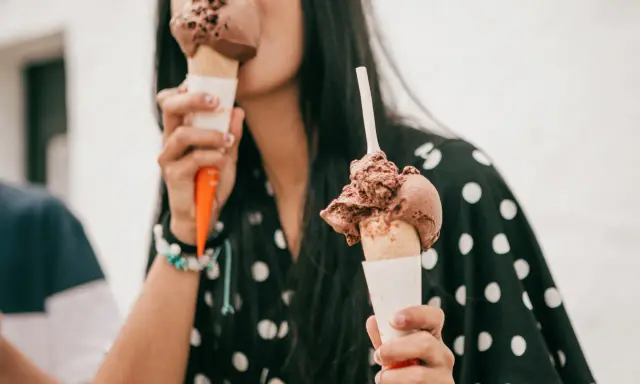 Una mujer disfruta de dos helados de chocolate, preguntándose quién inventó esta delicia.