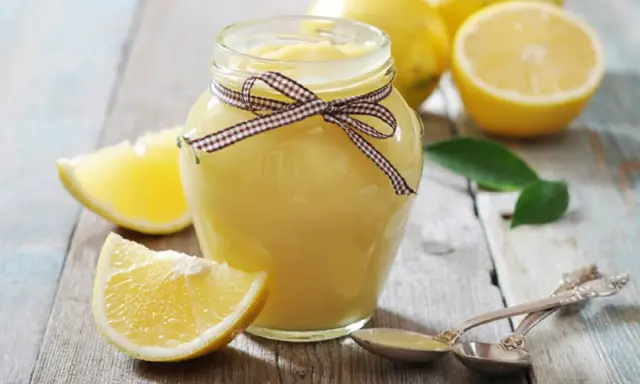 Tarro de lemon curd casero, decorado con un lazo, rodeado de limones frescos y rodajas.
