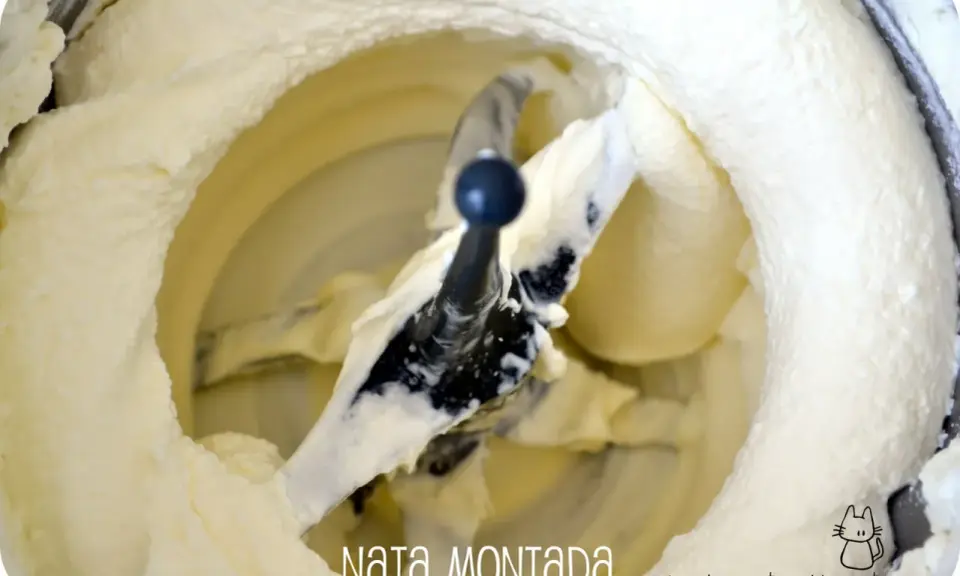 Batidora con pala mezclando nata montada, creando una textura esponjosa y cremosa, lista para postres.