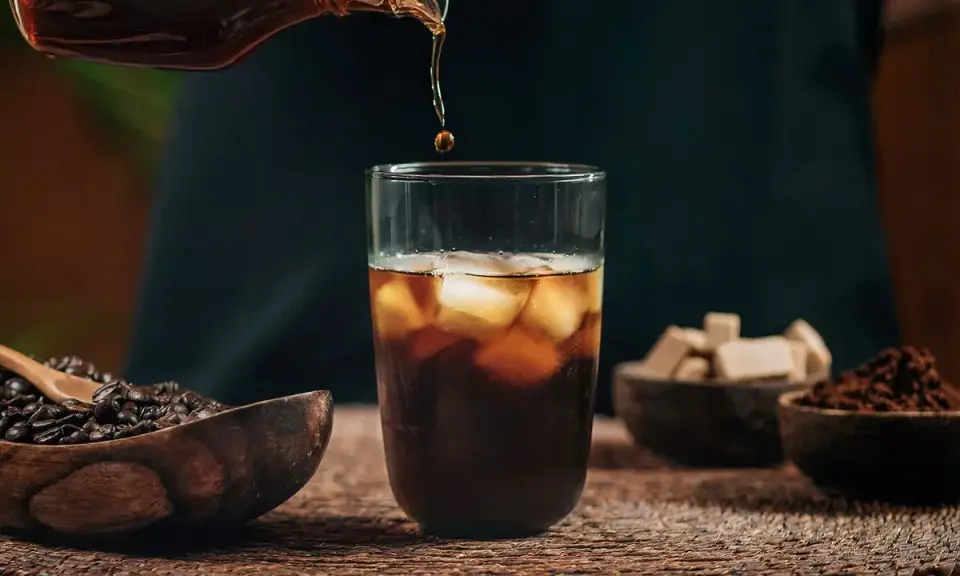 Un vaso de cold brew coffee con hielo, granos de café y cubos de azúcar.
