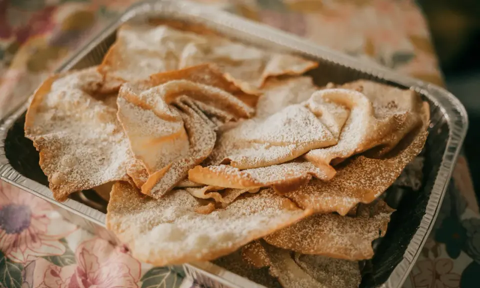 Orejas de carnaval espolvoreadas con azúcar glas en una bandeja metálica. ¡Perfectas para tu receta!