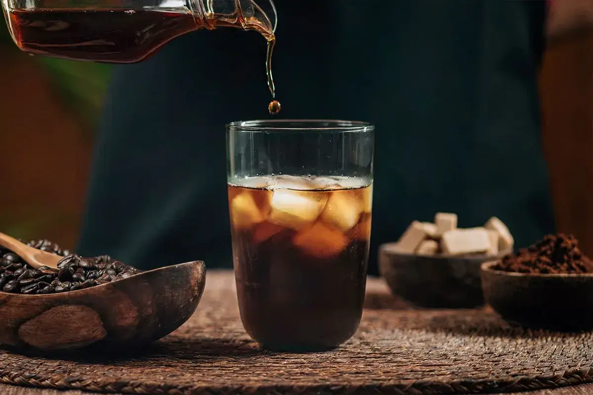 Un vaso de cold brew coffee con hielo, granos de café y cubos de azúcar.