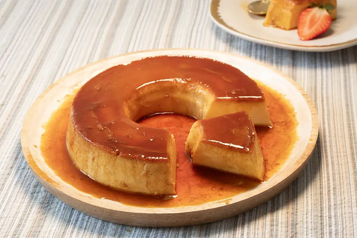 Flan de leche condensada con caramelo líquido, servido en plato de madera. Un trozo ha sido cortado.