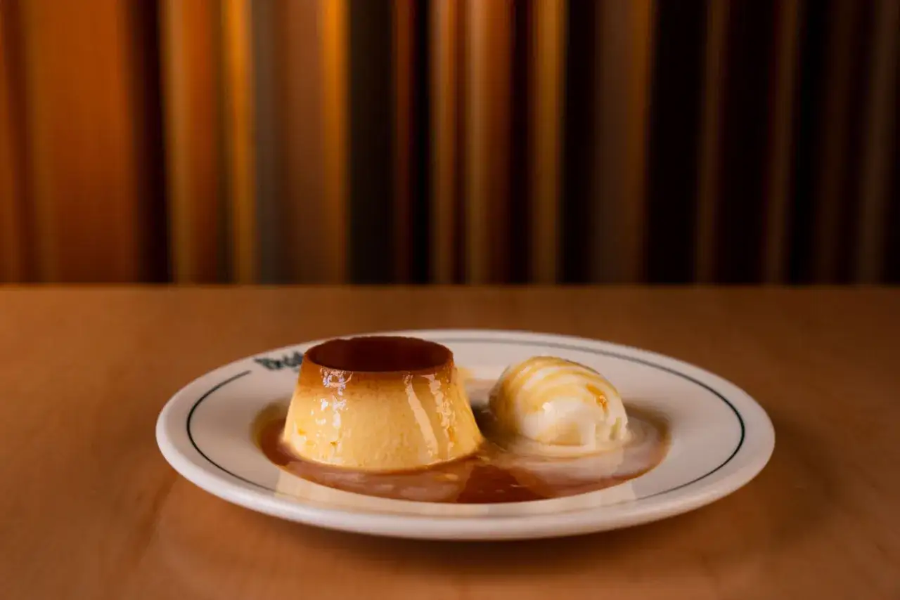 Un delicioso flan de hielo con caramelo líquido y una bola de helado cremoso, servido en un plato blanco con borde azul.