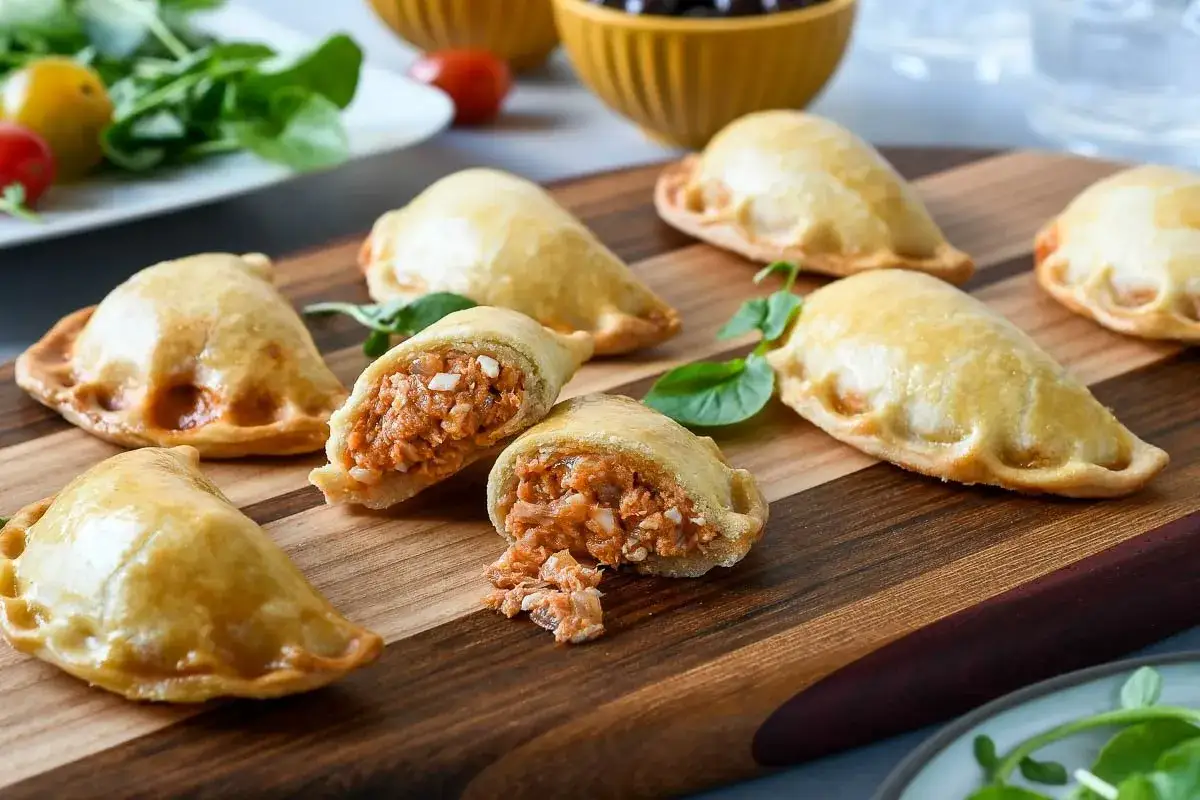 Empanadillas caseras doradas y crujientes, una rellena muestra su sabroso interior. Perfectas para compartir.