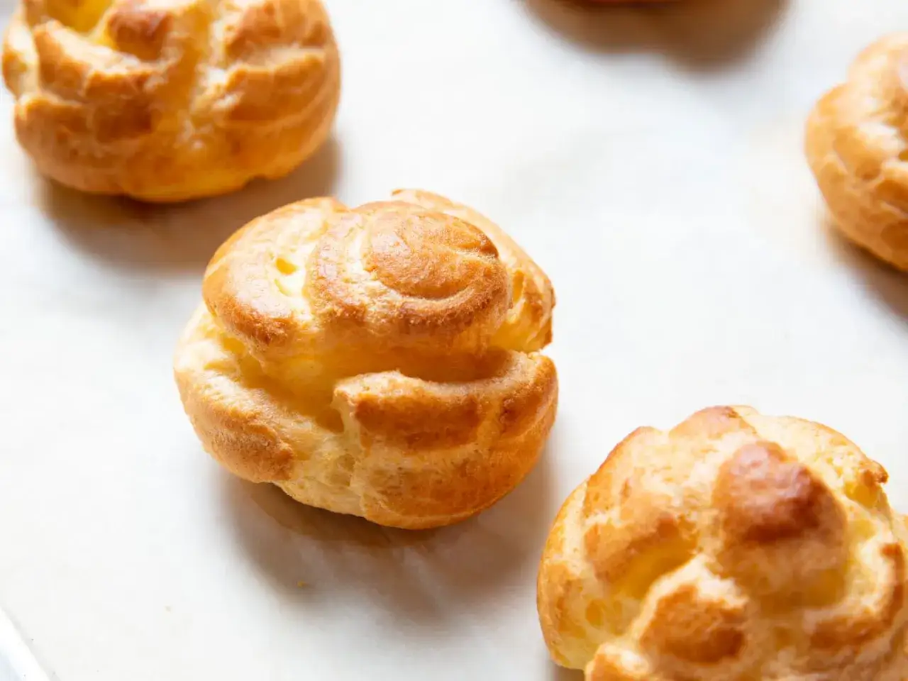 Bolas doradas de pasta choux recién horneadas, listas para rellenar con crema o helado.