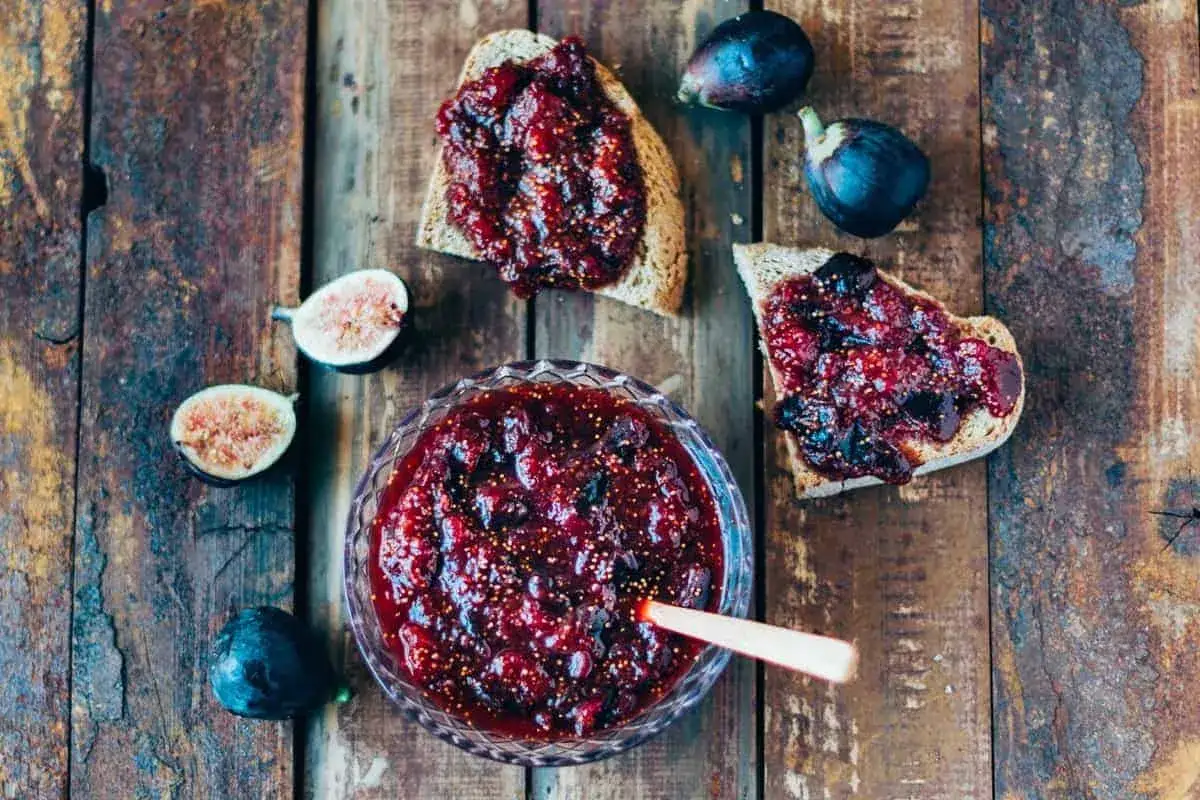 Un tazón de mermelada de higos casera, con tostadas untadas y higos frescos alrededor.