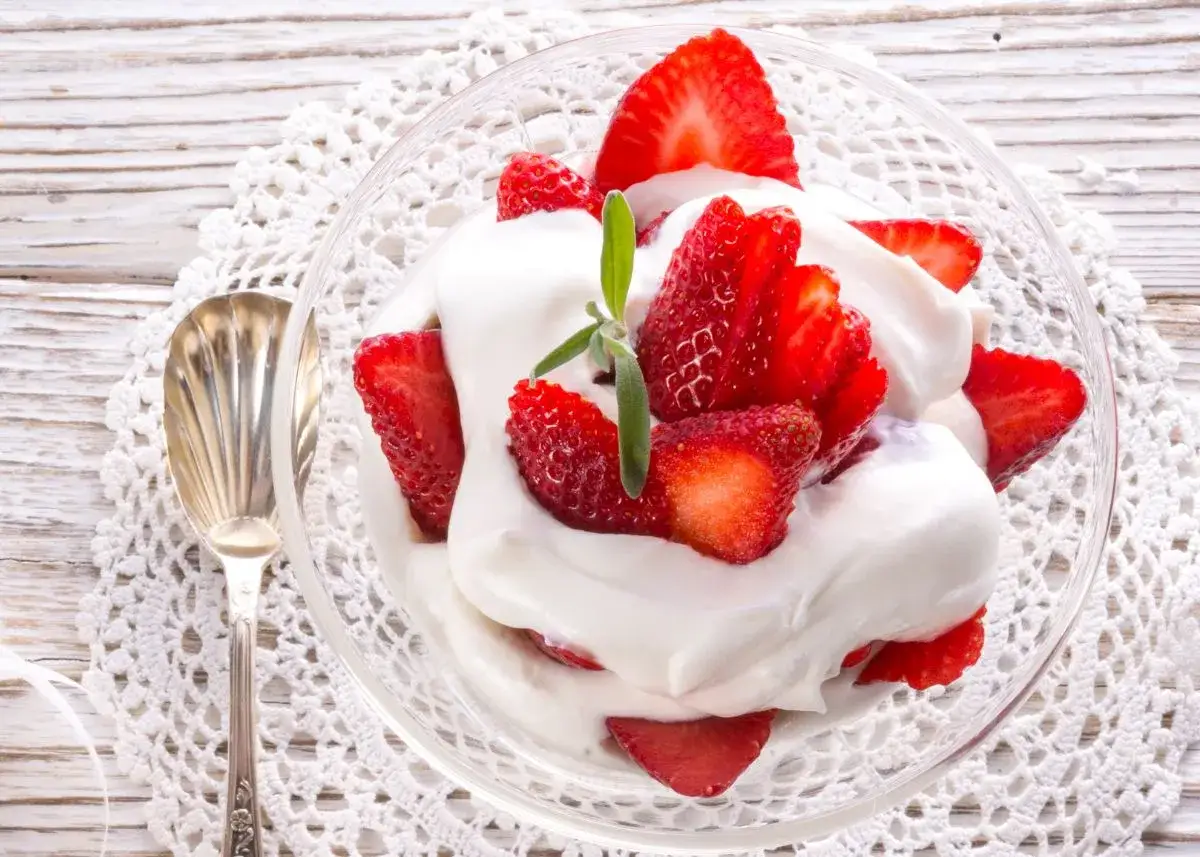 Fresas frescas con abundante nata montada en un cuenco de cristal, decorado con una ramita verde.