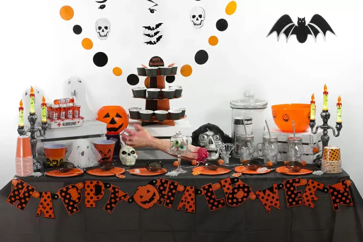Mesa de Halloween con decoración espeluznante y dulces típicos de Halloween. Hay calabazas, calaveras, fantasmas y murciélagos.