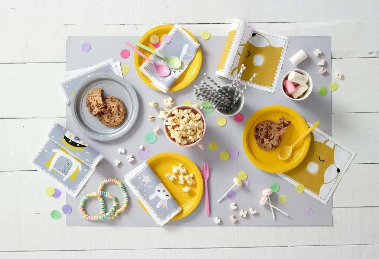 Mesa lista para una merienda de cumpleaños infantil: galletas, palomitas, dulces y servilletas con divertidos diseños de animales.