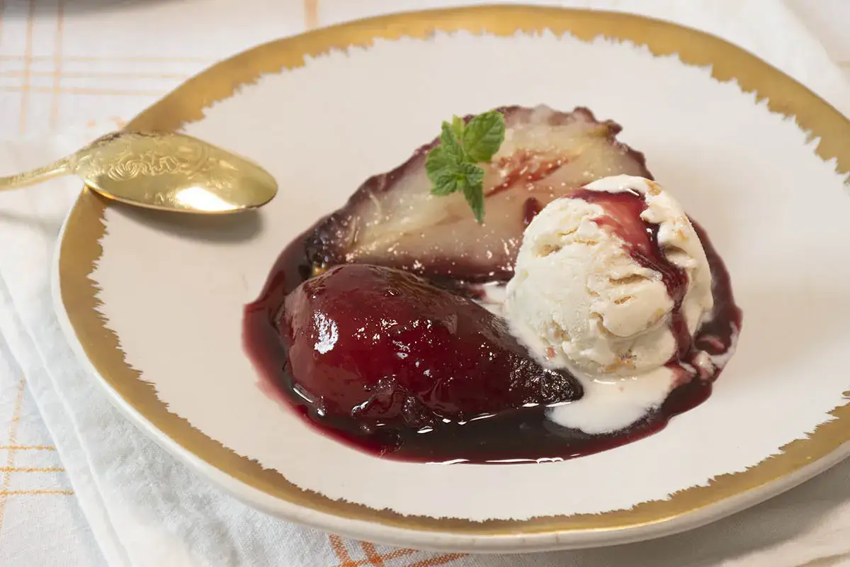 Peras al vino, tiernas y brillantes, acompañadas de helado cremoso y una hoja de menta. Un postre elegante.