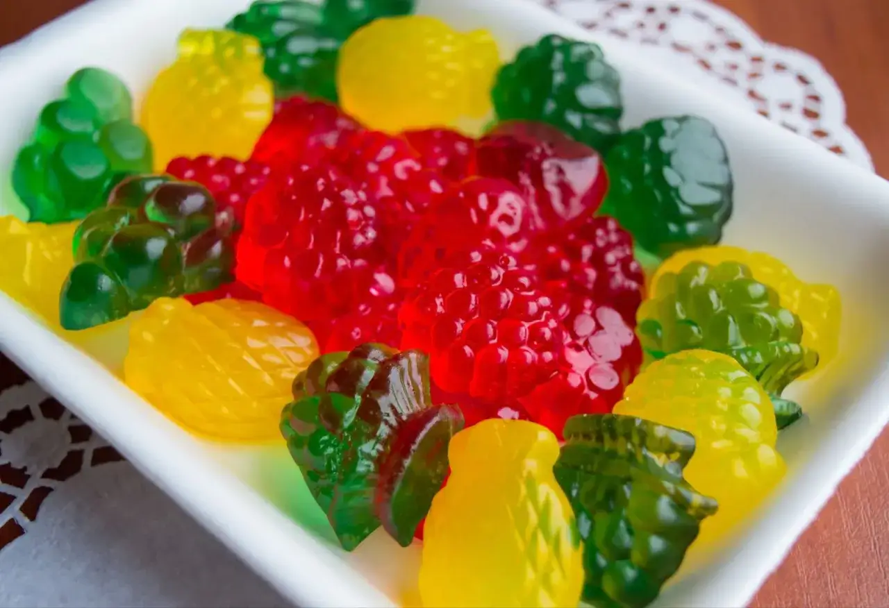 Un plato blanco lleno de chuches de colores: rojas con forma de frambuesa, verdes de uva y piña, y amarillas de piña. Así es como se hacen las chuches.