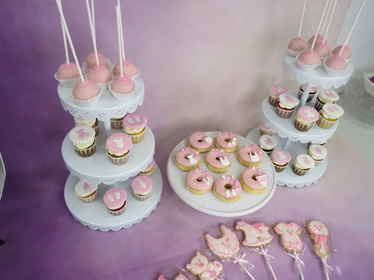 Mesa dulce baby shower con cake pops rosas, cupcakes decorados y galletas con motivos infantiles.