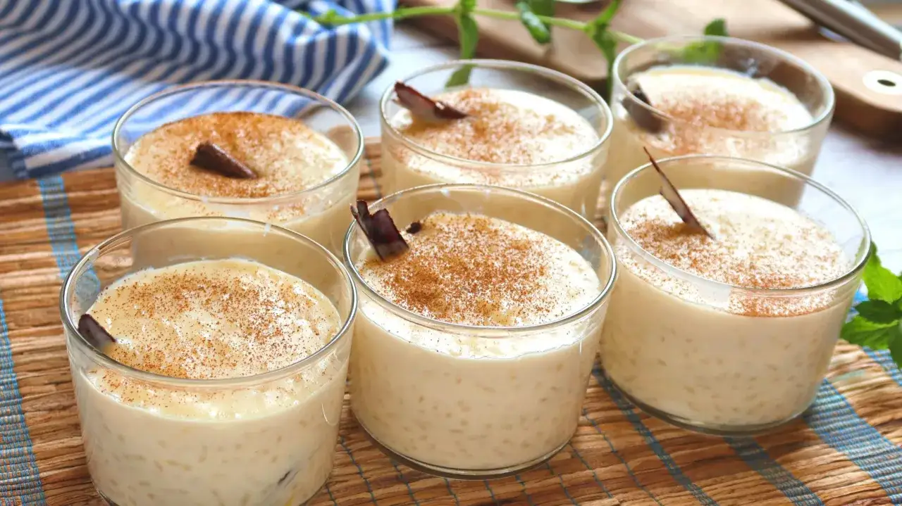Seis copas de cremoso arroz con leche, espolvoreado con canela y decorado con una rama de canela.