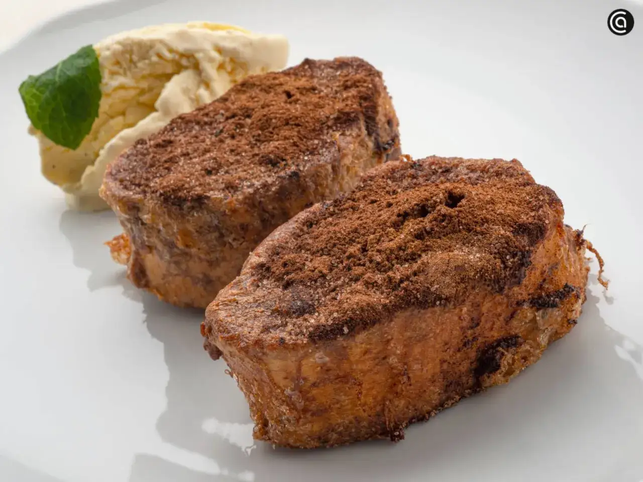 Dos deliciosas torrijas de chocolate espolvoreadas con cacao y azúcar, acompañadas de helado de vainilla y una hoja de menta.