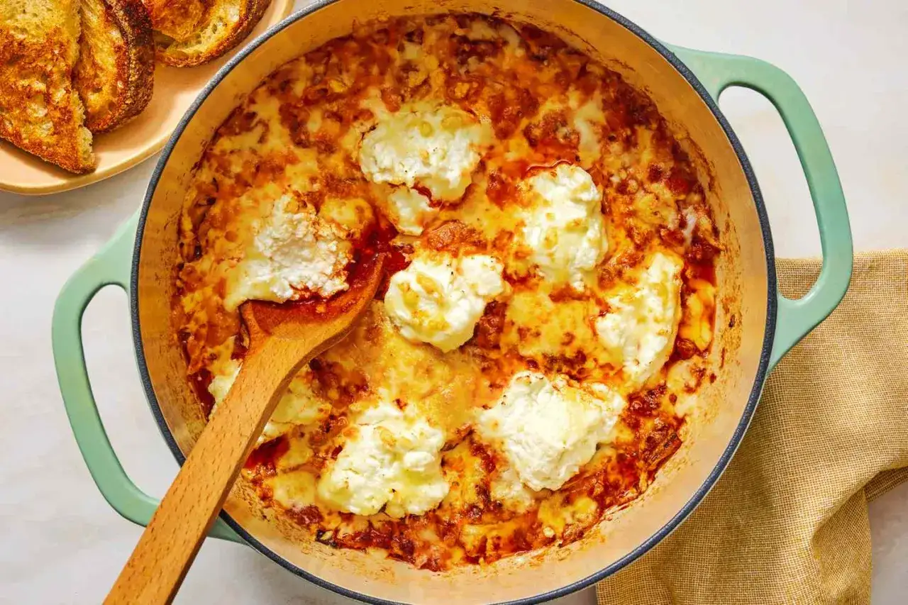 Delicioso plato horneado con queso ricotta y salsa de tomate, perfecto para recetas con pocos ingredientes. Servido con pan tostado.