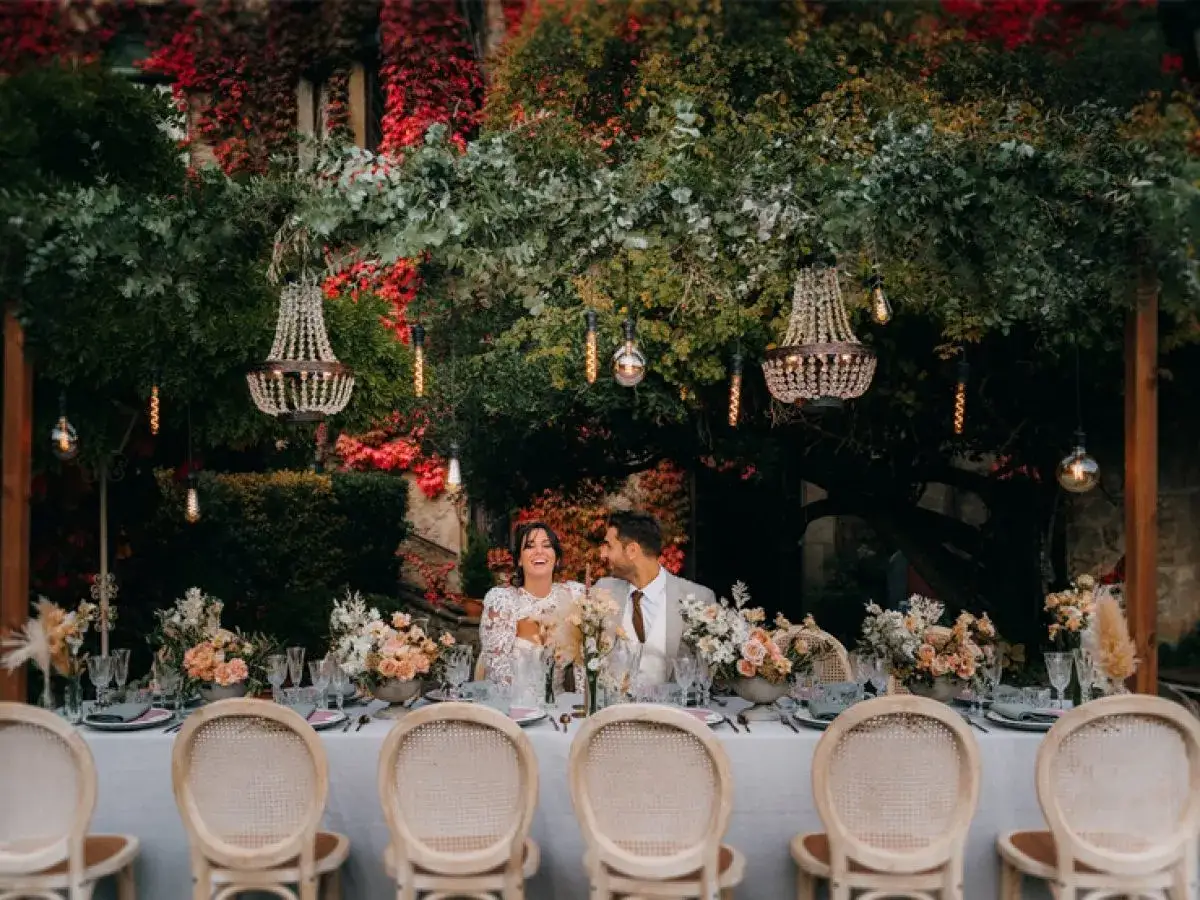 Una romántica mesa dulce boda bajo un dosel de hojas y luces, con una pareja sonriente.