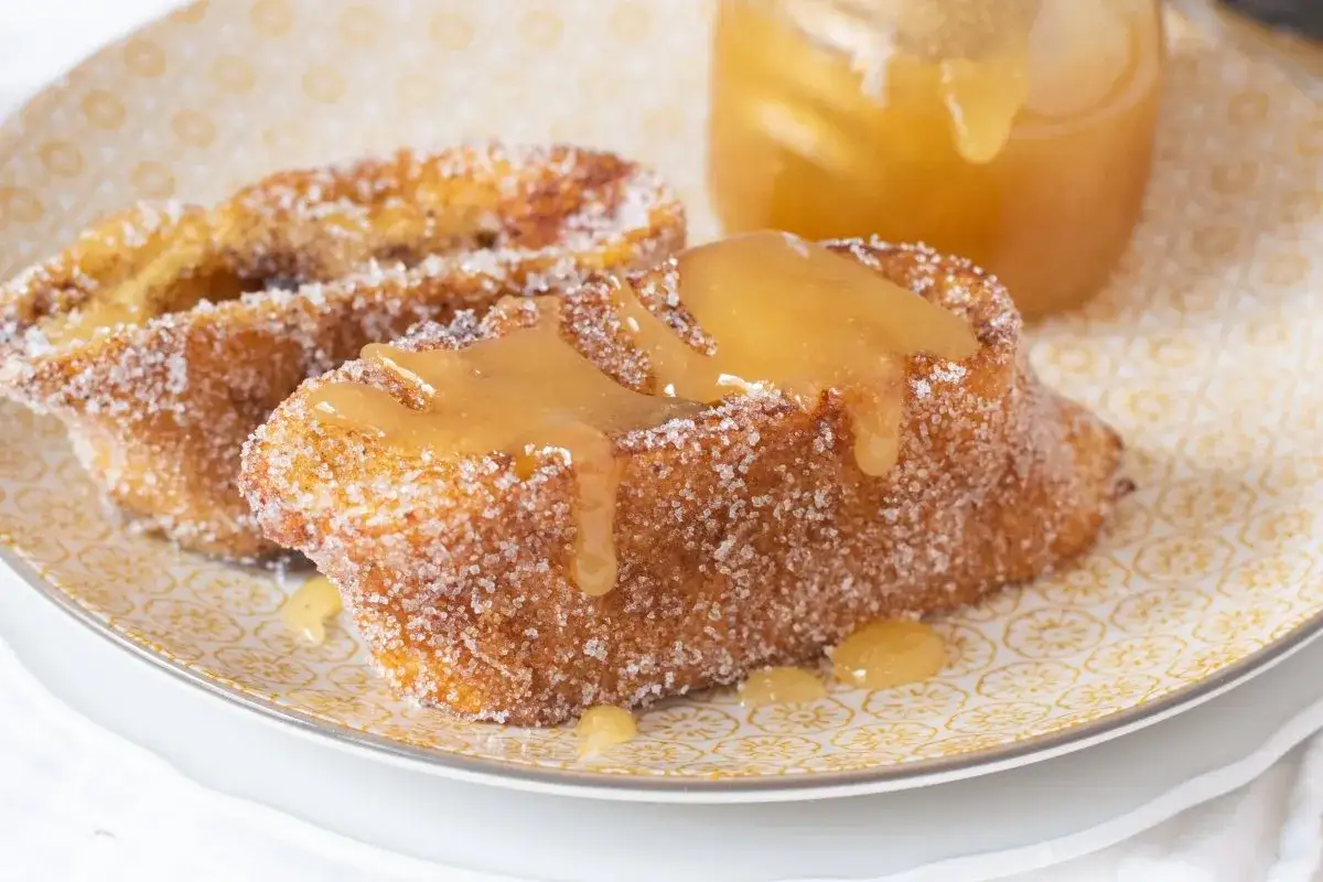 Torrijas de miel, doradas y rebozadas en azúcar, con un chorrito de miel dorada cayendo.