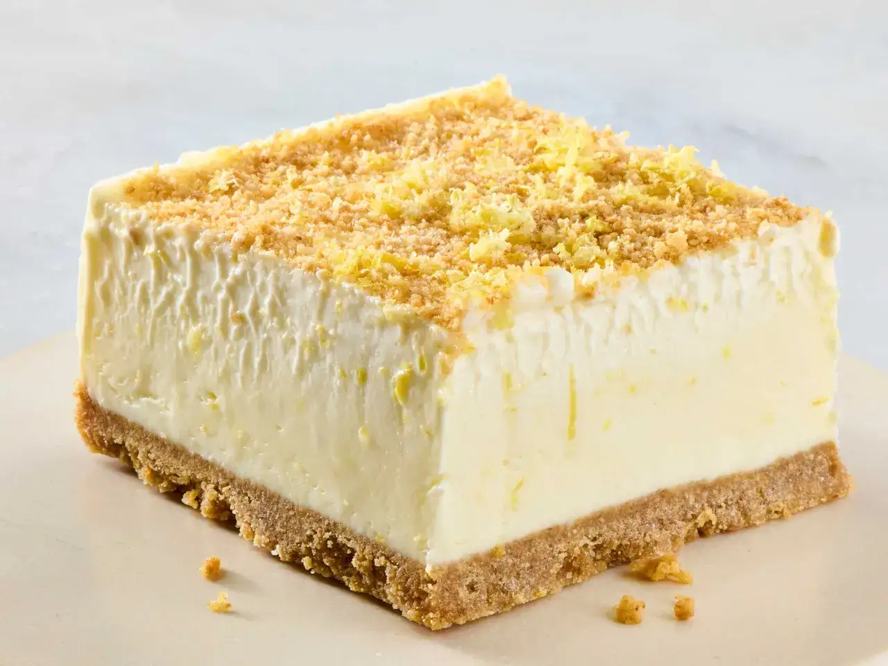 Rebanada de postre de limón con base de galletas, cubierta con migas crujientes y ralladura de limón.