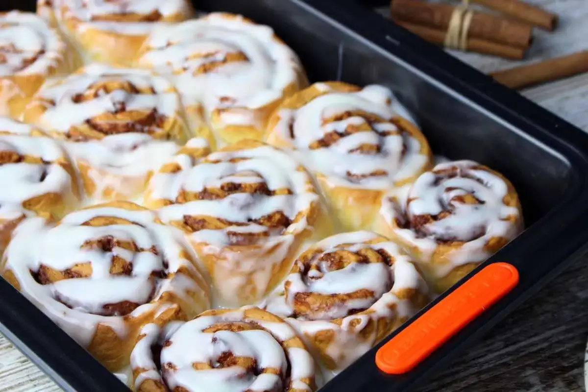 Rollo de canela recién horneados, cubiertos con glaseado blanco cremoso, listos para disfrutar.