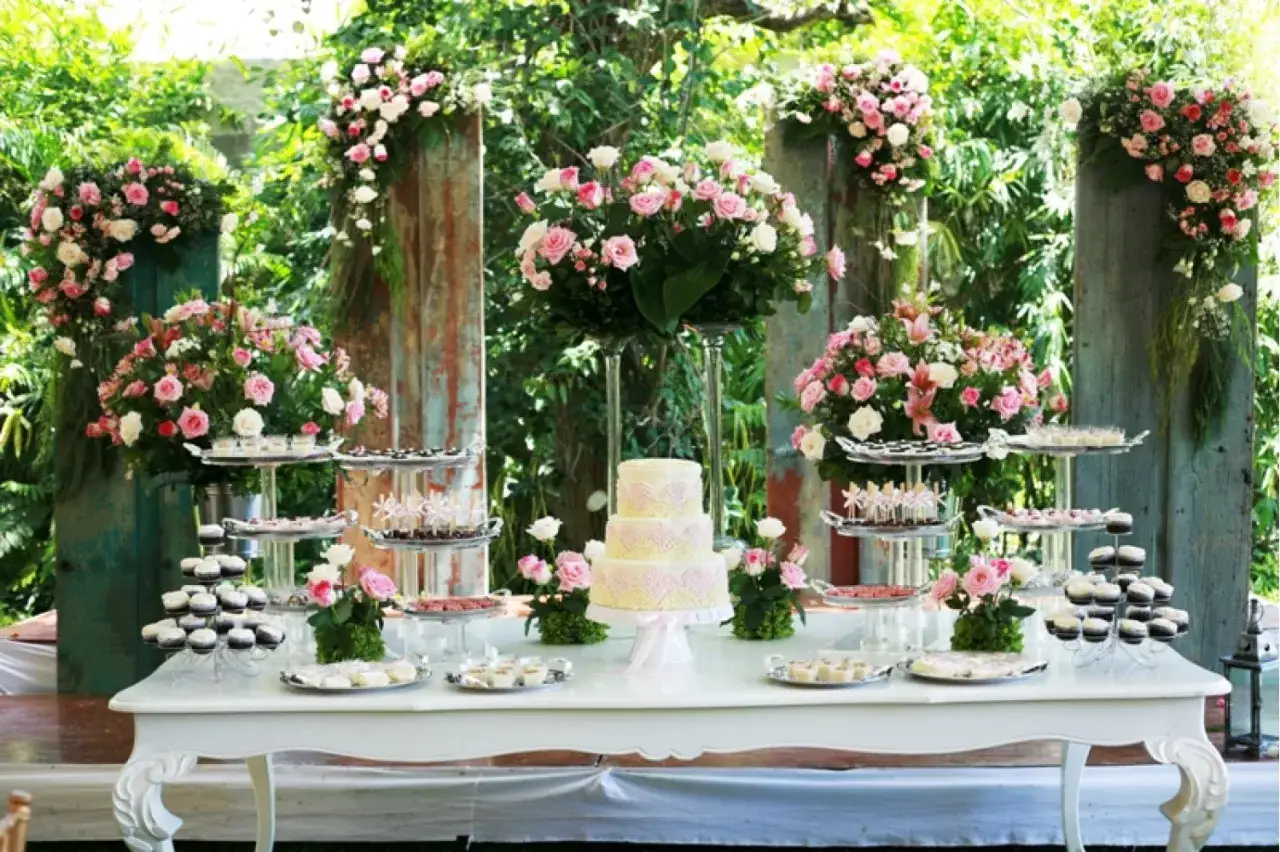 Mesa de dulces y pastel de tres pisos, decorada con abundantes flores rosas y blancas. Un festín visual para unas mesas comunion inolvidables.