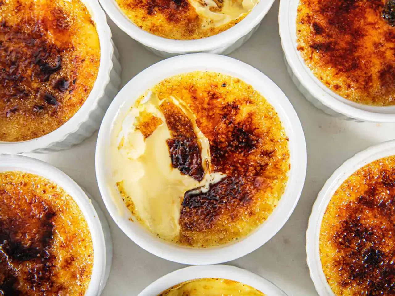 Varios creme brulee en sus recipientes blancos, con la capa de azúcar caramelizada dorada y crujiente, listos para ser disfrutados.