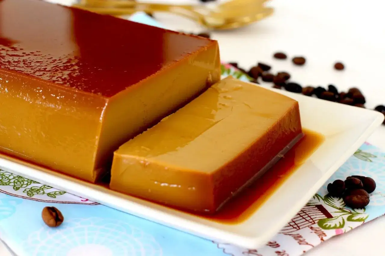 Un delicioso flan de café, con su caramelo brillante, servido en una bandeja blanca. Granos de café tostado decoran la escena.