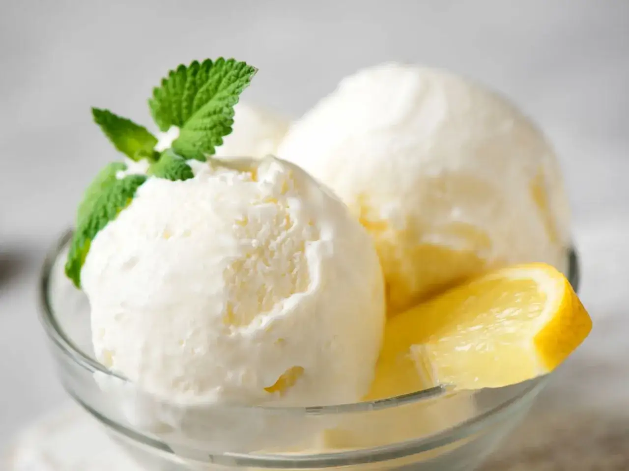 Delicioso helado de limón casero, servido en un cuenco de cristal con hojas de menta y rodajas de limón fresco.