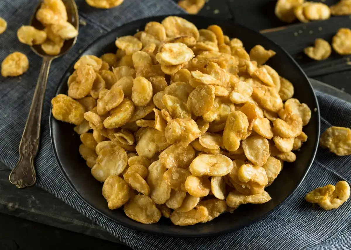 Un plato lleno de crujientes habas fritas, doradas y listas para disfrutar. Una cuchara a la izquierda muestra más de este delicioso aperitivo.