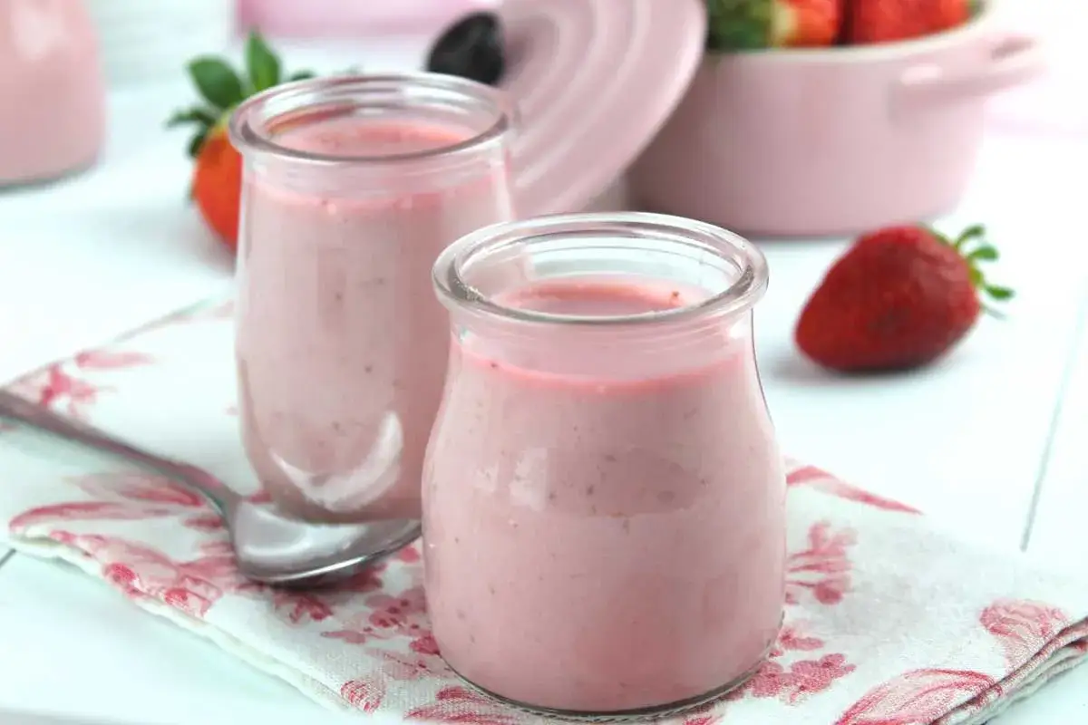 Dos vasitos de petit suisse de fresa casero sobre una servilleta floral, con fresas frescas al fondo.