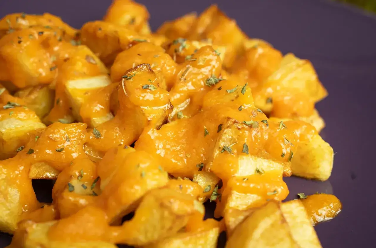 Patatas bravas receta: crujientes patatas cubiertas con una salsa brava cremosa y especiada, espolvoreadas con hierbas frescas.