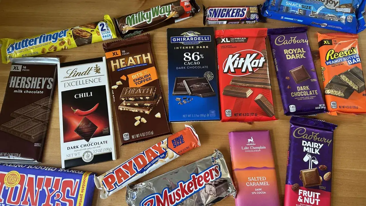Variedad de chocolatinas famosas, incluyendo Hershey's, KitKat, Reese's, Snickers, y más, listas para disfrutar.