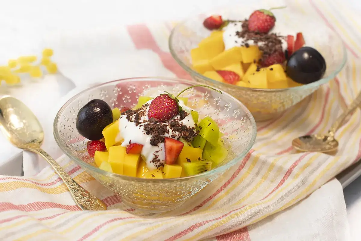 Dos copas de frutas frescas con yogur y chocolate rallado, deliciosas golosinas saludables.