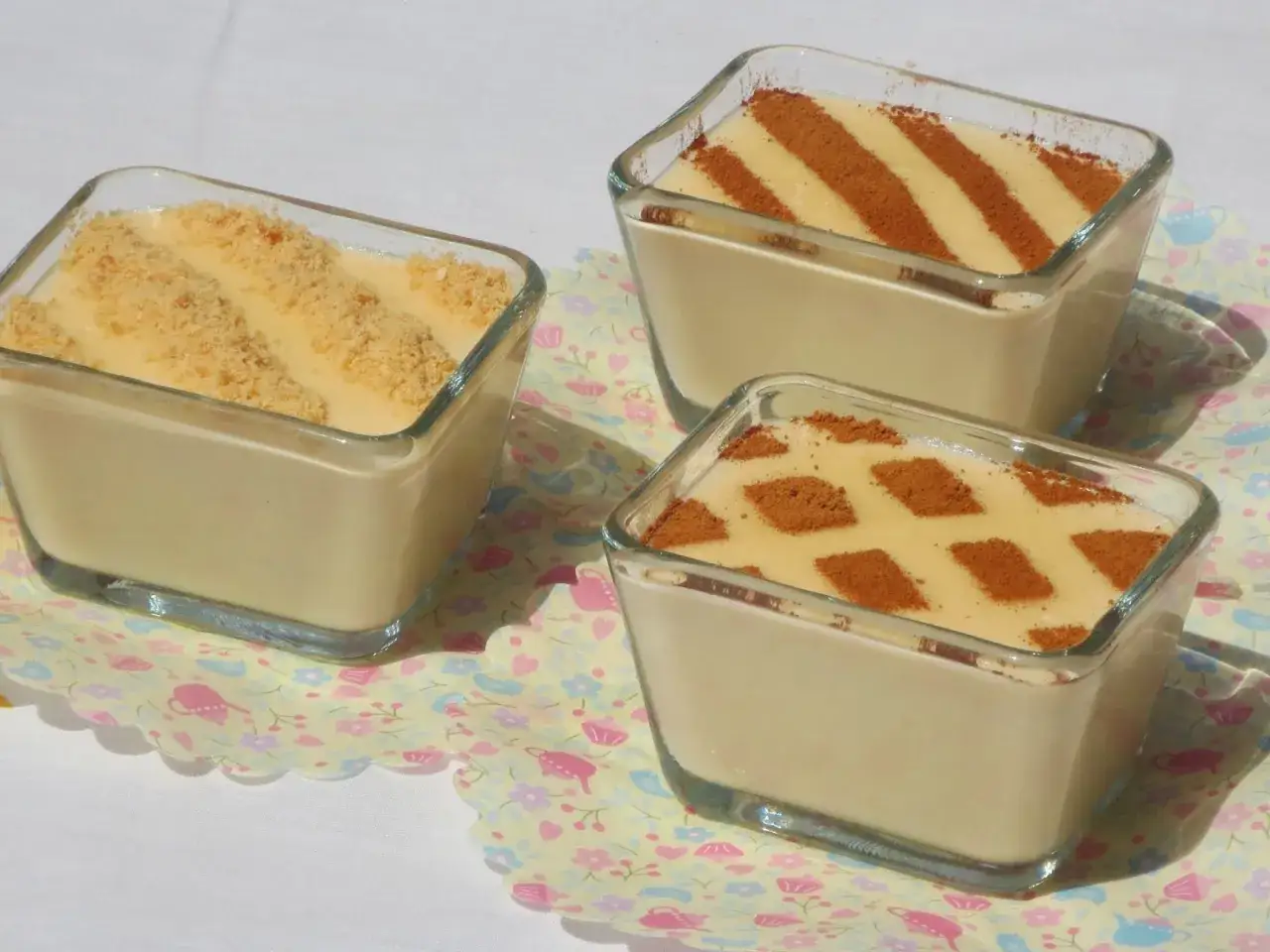 Deliciosas natillas Thermomix en vasitos de cristal, una con galleta triturada y otras dos con canela formando rombos y rayas.