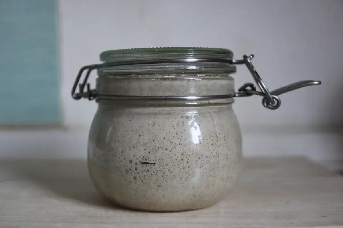 Tarro de vidrio con masa madre burbujeante, lista para hacer pan. El proceso de hacer masa madre es un arte.